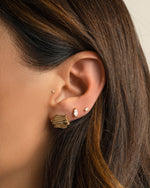 Gold earring stack featuring minimalist scribble stud earrings, a marquise cut diamond stud and a small stud earring to follow on models ear