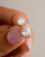 Dainty gold earrings being held between two fingers