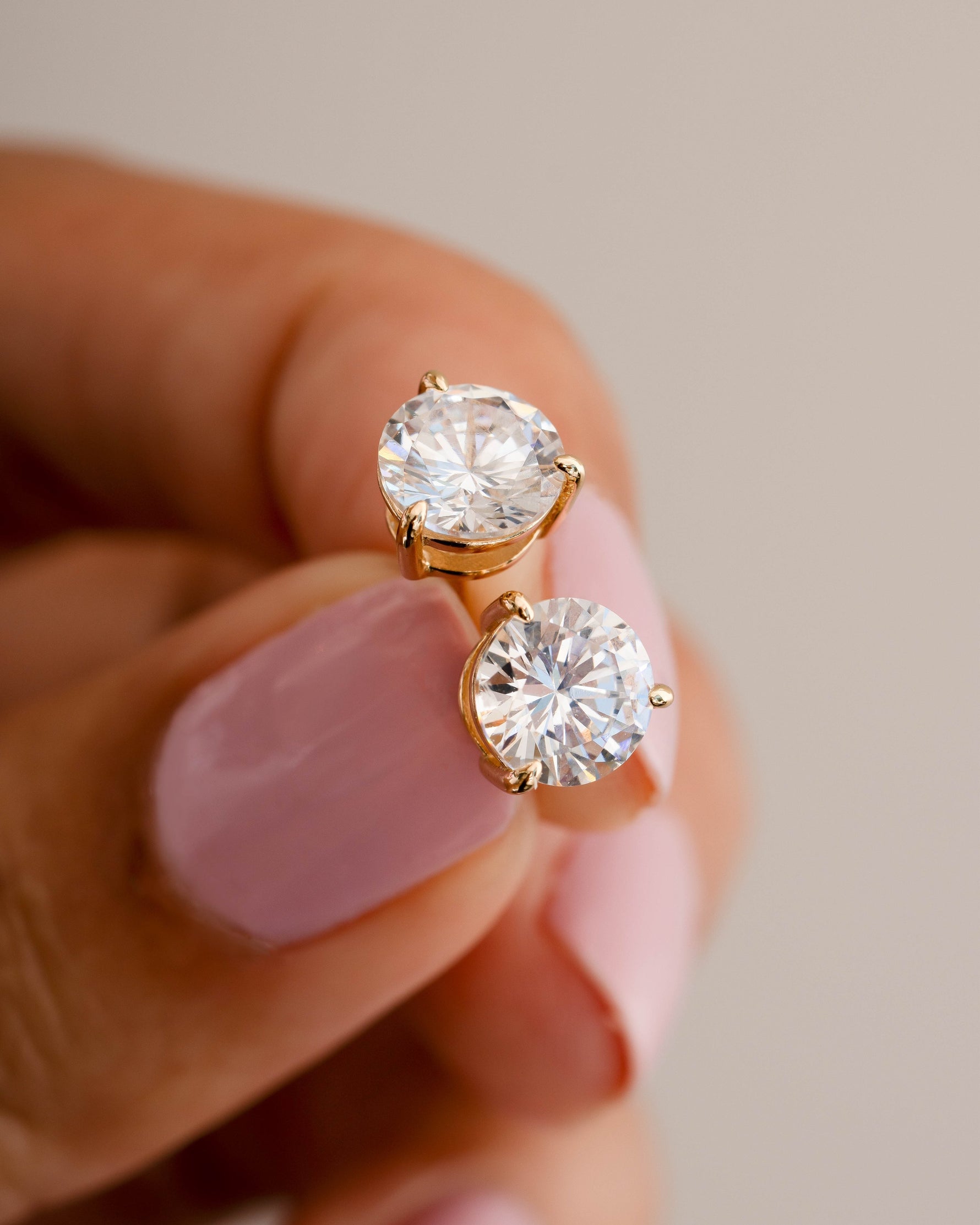 Dainty gold earrings being held between two fingers