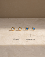 White cubic zirconia studs and march birthstone earrings on a marble background with text depicting the gemstone