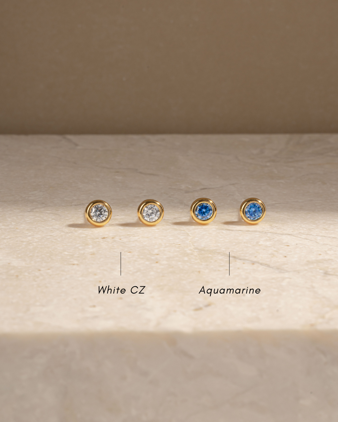 White cubic zirconia studs and march birthstone earrings on a marble background with text depicting the gemstone