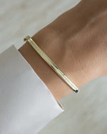 Gold stackable bracelet featuring a bangle design with cz stones on a wrist with a light background