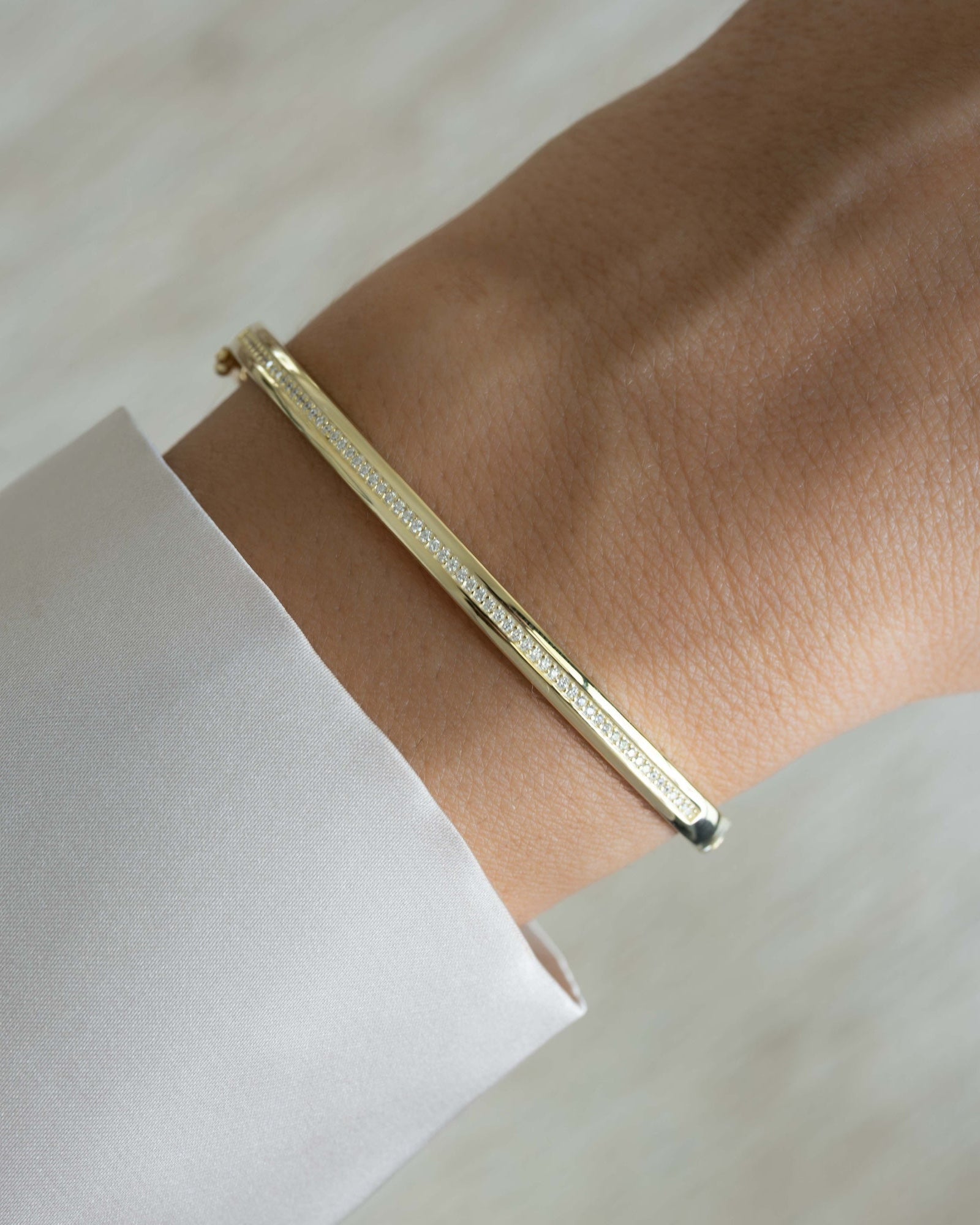 Gold stackable bracelet featuring a bangle design with cz stones on a wrist with a light background
