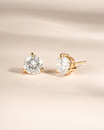 Gold stud earrings with round solitaire gemstones on a beige background