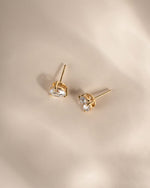 Dainty gold diamond statement earrings on a neutral background