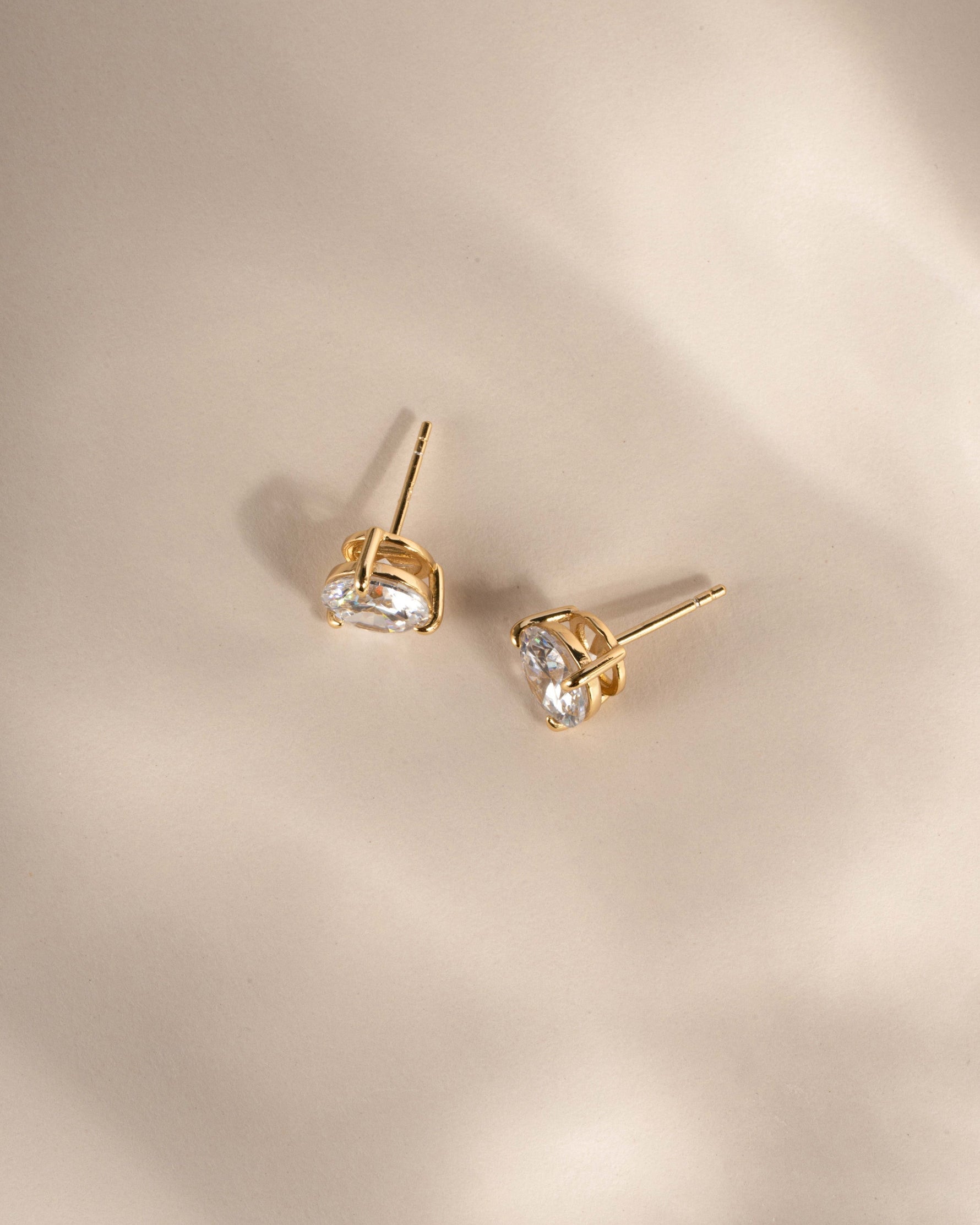 Dainty gold diamond statement earrings on a neutral background