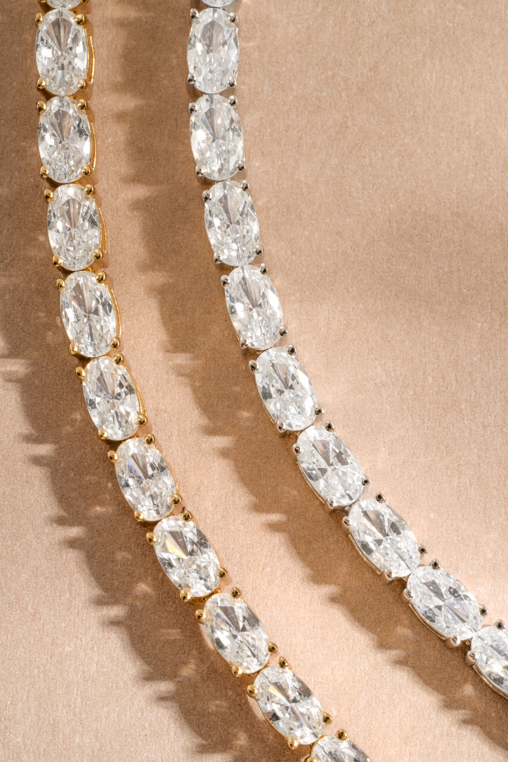 Gold diamond bracelets laying on a neutral background, one sterling silver bracelet, and one gold plated bracelet
