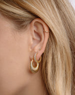 Close-up of a person wearing gold hoop earrings, diamond huggie hoops, and a bezel stud earring 