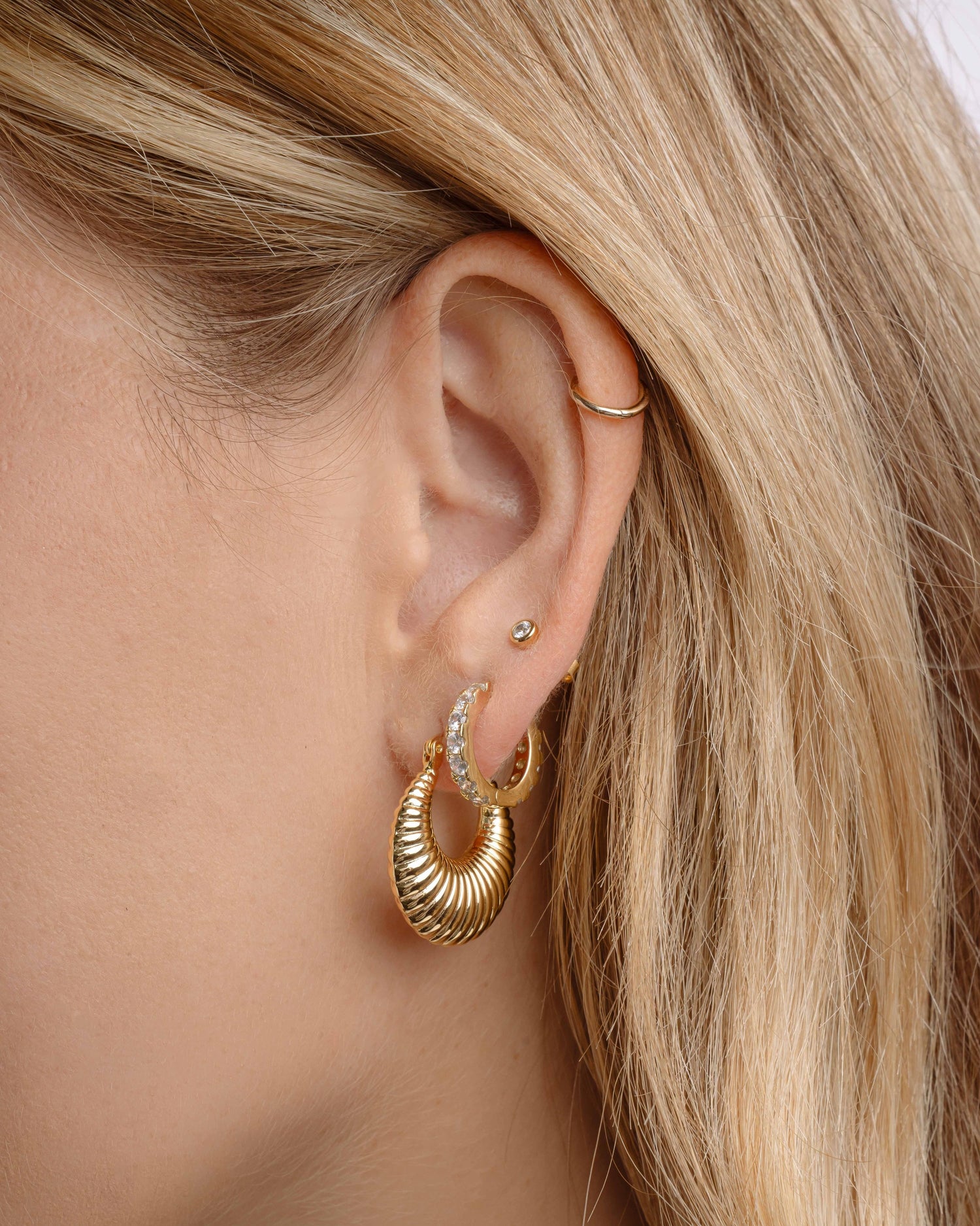 Close-up of a person wearing gold hoop earrings, diamond huggie hoops, and a bezel stud earring 