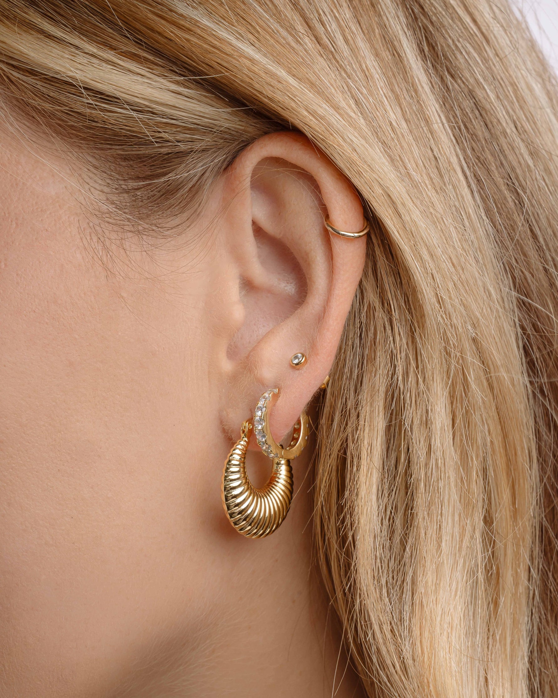 Close-up of a person wearing gold hoop earrings, diamond huggie hoops, and a bezel stud earring 