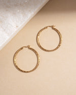 Flatlay of 35mm gold textured hoop earrings with hammered twisted finish, lightweight vintage-inspired hoops for daily wear.