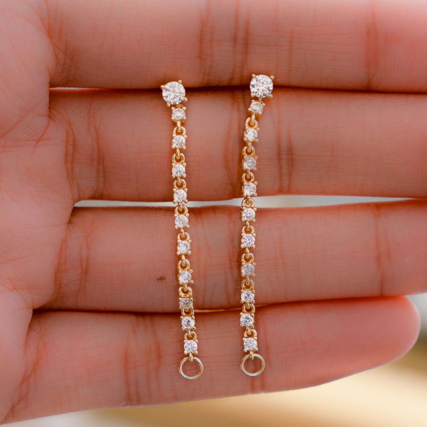 Model holding gold chain earrings in her palm, showing its dangle earring charm.