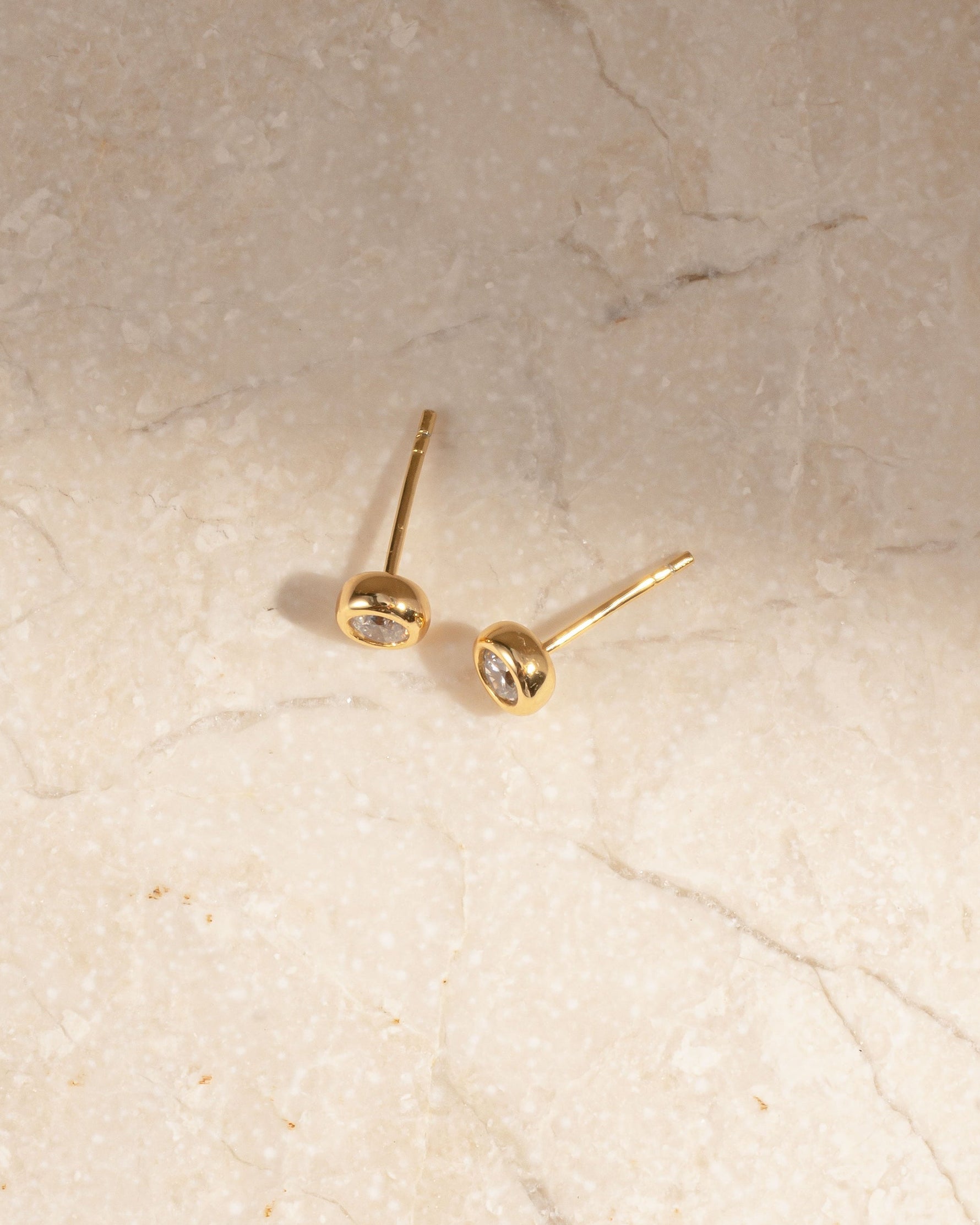 Gold small stud earrings on a marble background