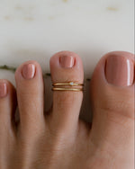 Gold body jewelry featuring an adjustable toe ring with a cubic zirconia bezel set stone on model