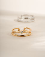 Gold foot jewelry featuring a minimalist toe ring and a silver toe ring blurred in the background