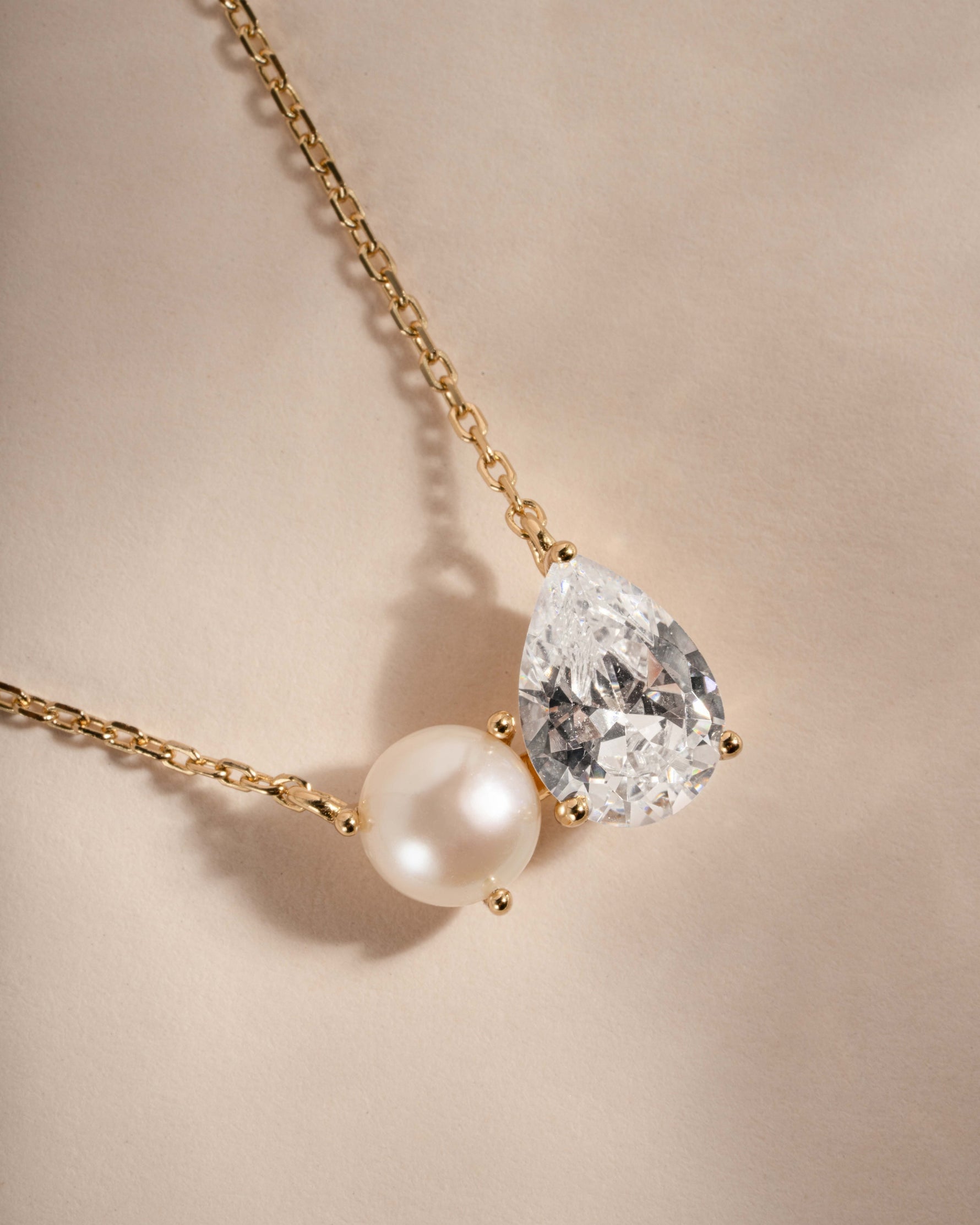 Necklace with teardrop-shaped diamond and pearl on a beige background