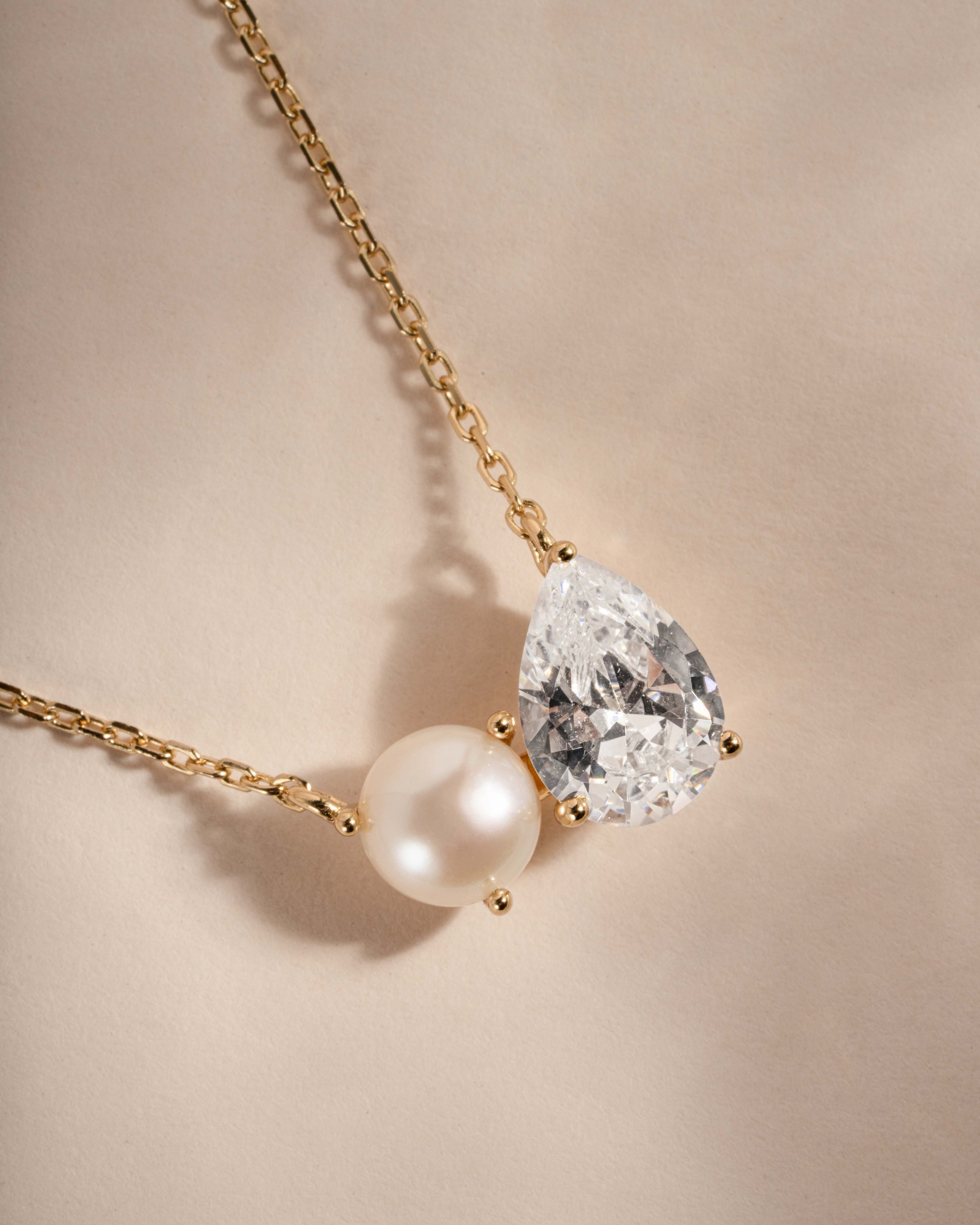 Necklace with teardrop-shaped diamond and pearl on a beige background