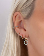 Close-up of a model wearing turquoise huggie earrings, small gold hoops, a minimalist stud earring and a turquoise ear cuff
