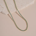 flatlay of gold tennis necklace with turquoise stones and a round bezel design