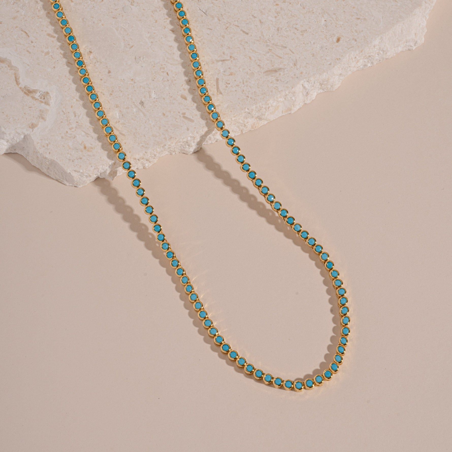 flatlay of gold tennis necklace with turquoise stones and a round bezel design