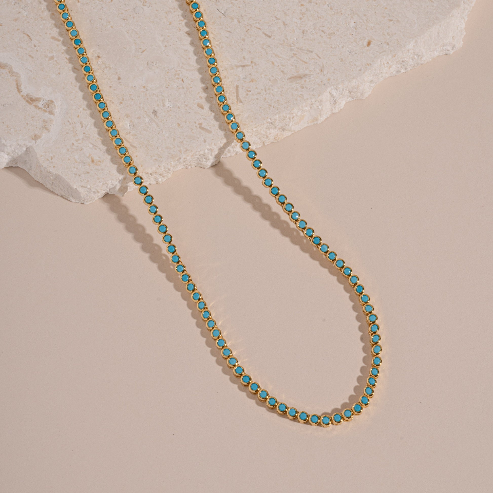 flatlay of gold tennis necklace with turquoise stones and a round bezel design