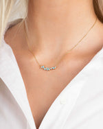 Gold turquoise gemstone bar necklace with small stones worn by a person in a white shirt
