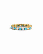 Gold eternity ring with turquoise and white cz gemstones on a white background
