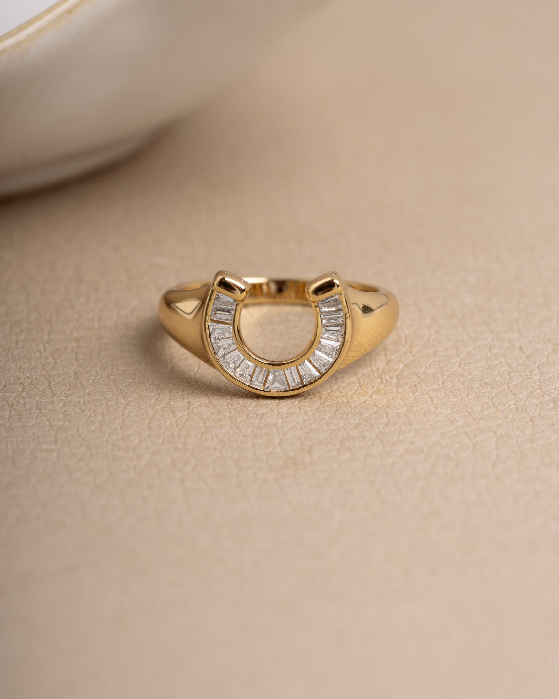 Gold baguette ring with a horseshoe design on a plain background