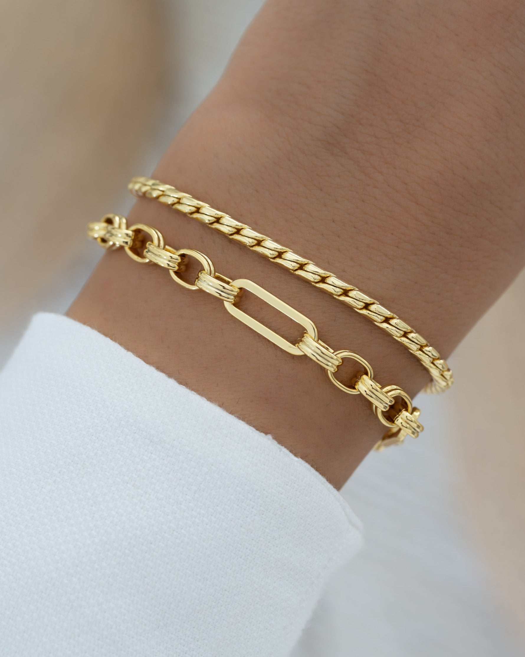 Gold chain bracelet stack on a wrist with a plain background