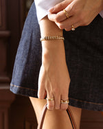 Closeup image of model wearing gold chain tennis bracelet with cubic zirconia diamonds and gold stackable rings