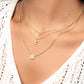 model wearing gold halo cut emerald necklace, tiny cross necklace, and tiny gold solitaire diamond necklace.