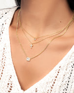 model wearing gold halo cut emerald necklace, tiny cross necklace, and tiny gold solitaire diamond necklace.