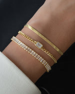 model wearing gold bracelet stak featuring herringbone bracelet, baguette tennis bracelet and a cuban link emerald cut bracelet