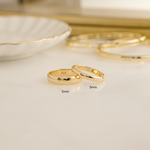 close up of two gold wedding bands in two different sizes, one thick and one that is thinner for a his and hers look