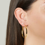 model wearing gold earring stack featuring gold hoop earring, a three stone cluster stud earring, and a three stone cluster tiny studs