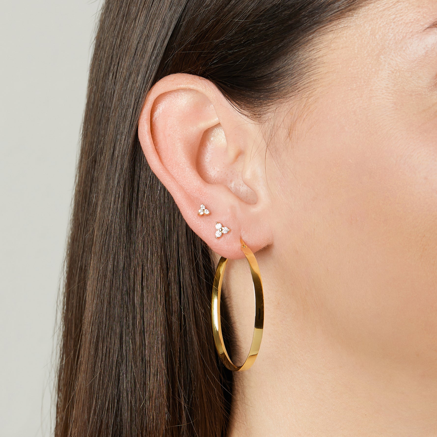 model wearing gold earring stack featuring gold hoop earring, a three stone cluster stud earring, and a three stone cluster tiny studs