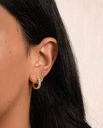 model wearing studded huggie hoop earrings, mini pave hoops and a solitaire stud in gold