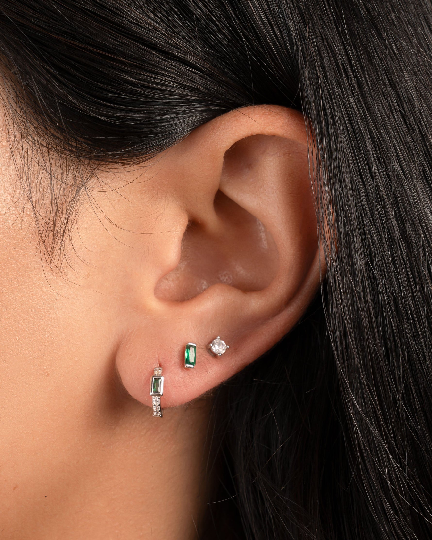 model wearing sterling silver earring stack featuring emerald huggie hoops, a emerald baguette stud earring, and a solitaire stud earring
