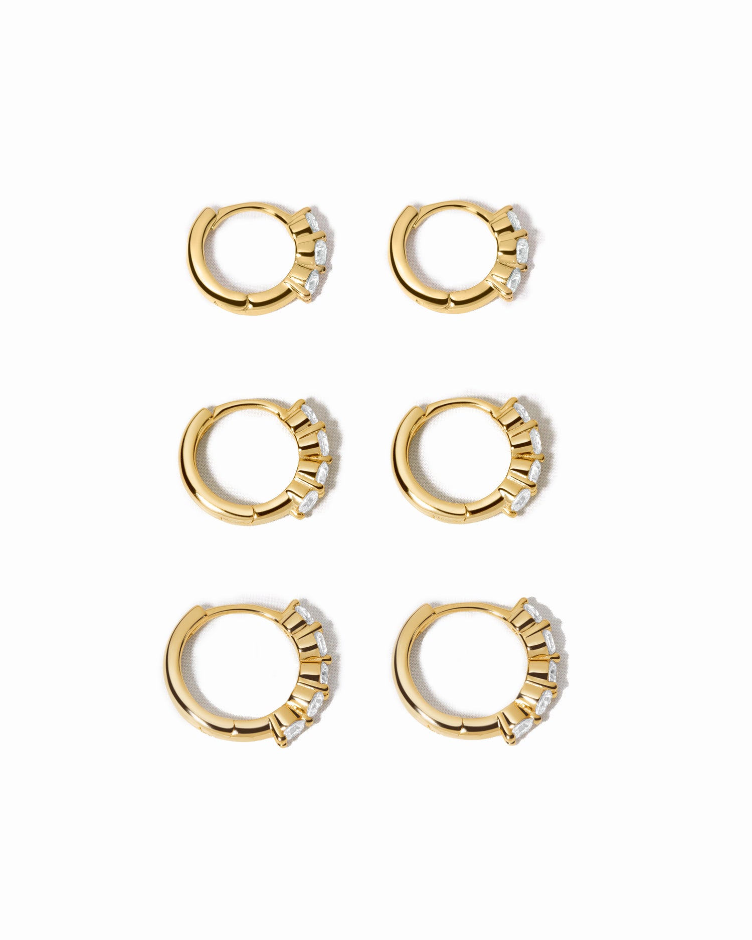 Set of gold hoop earrings with small diamonds on a white background
