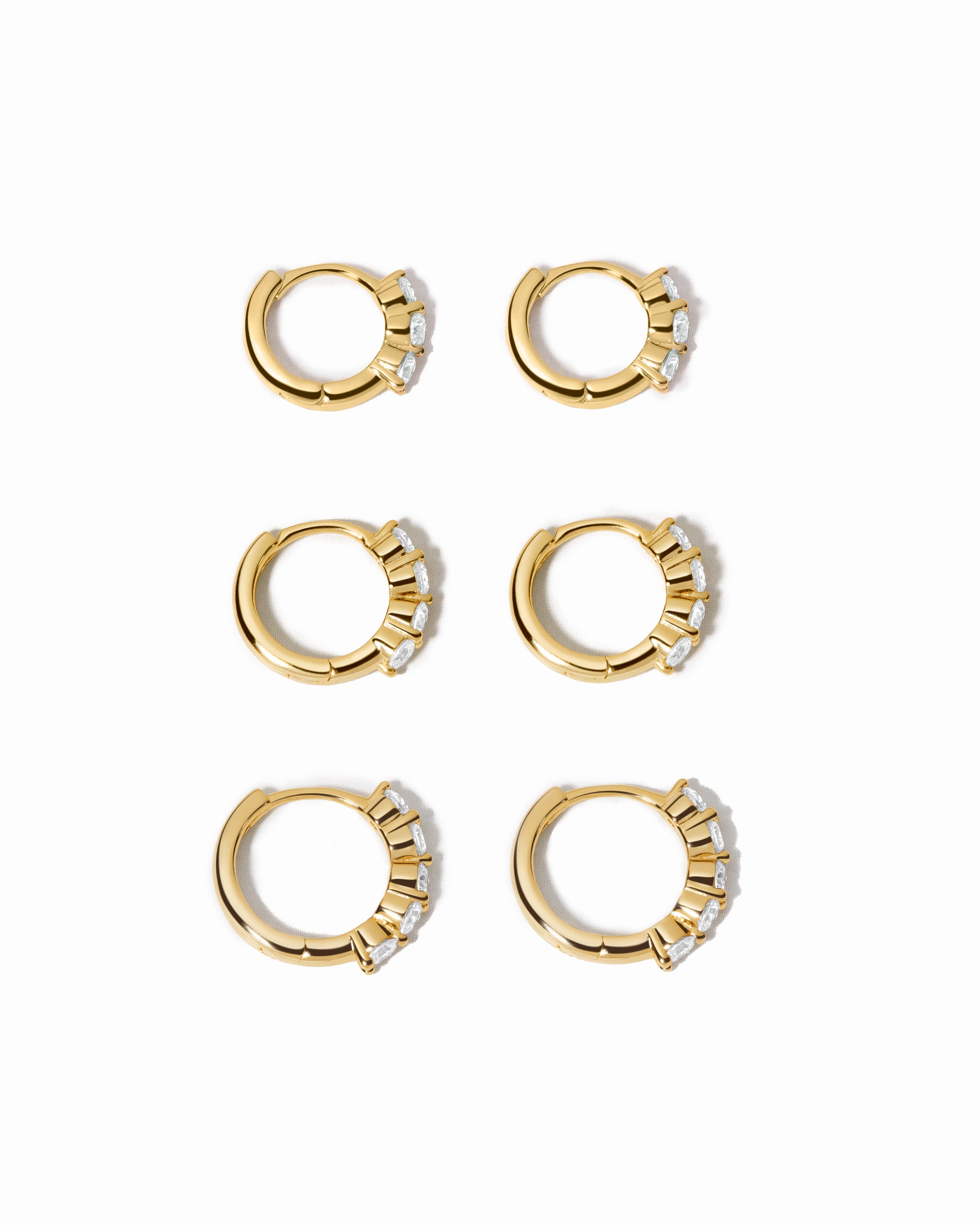 Set of gold hoop earrings with small diamonds on a white background
