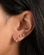 model wearing gold ear stack featuring a dainty emerald green huggie with a baguette stone in the center, a baguette stud earring in emerald, and a white cz stud earring in her third hole