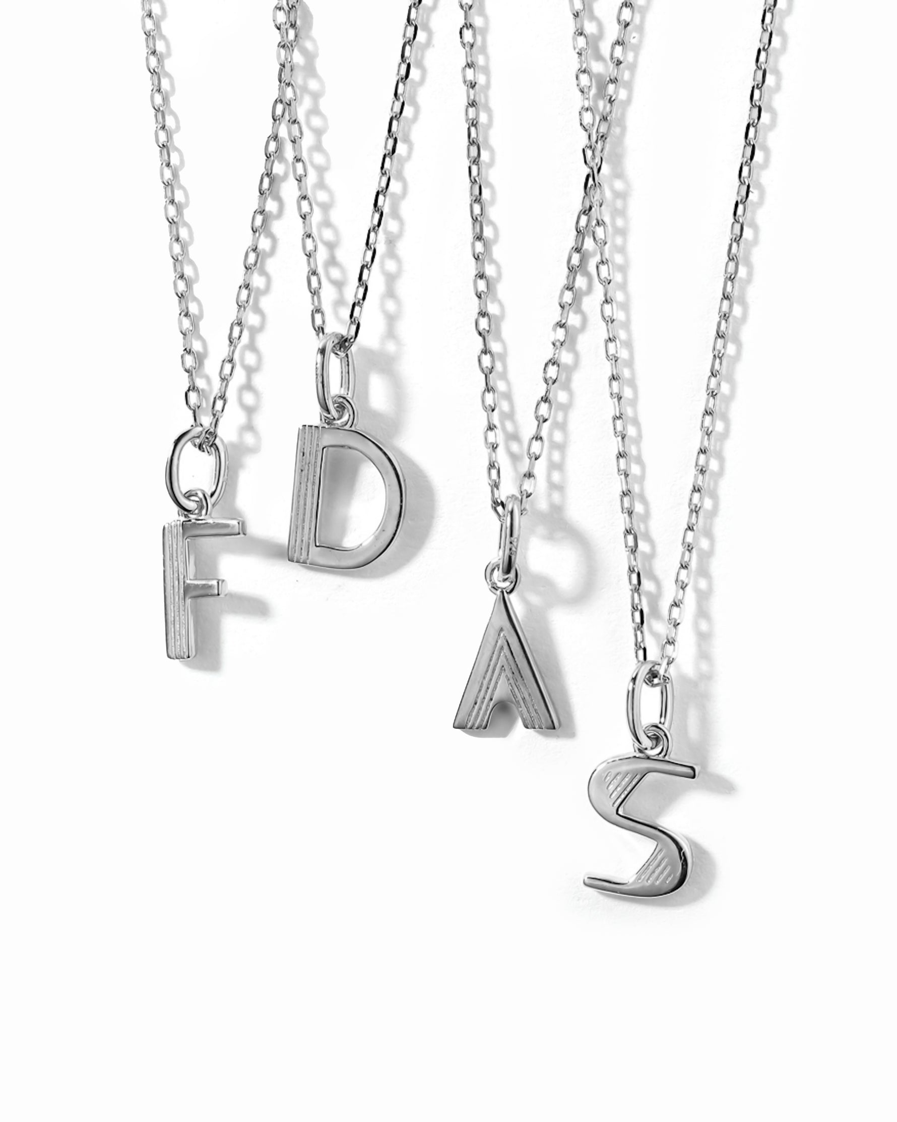 silver custom jewelry featuring different silver initial necklaces on a white background