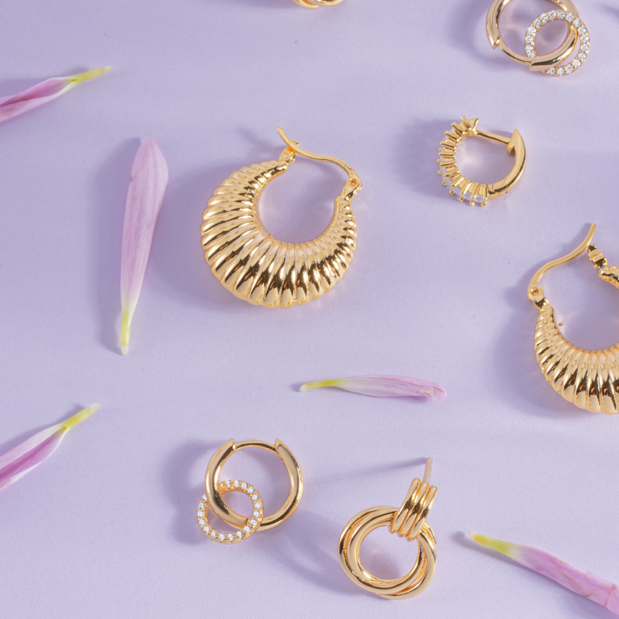 Gold hoop earrings on a light purple background with pink flower petals