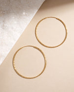 Pair of 53mm gold hoop earrings with diamond detail on a beige background