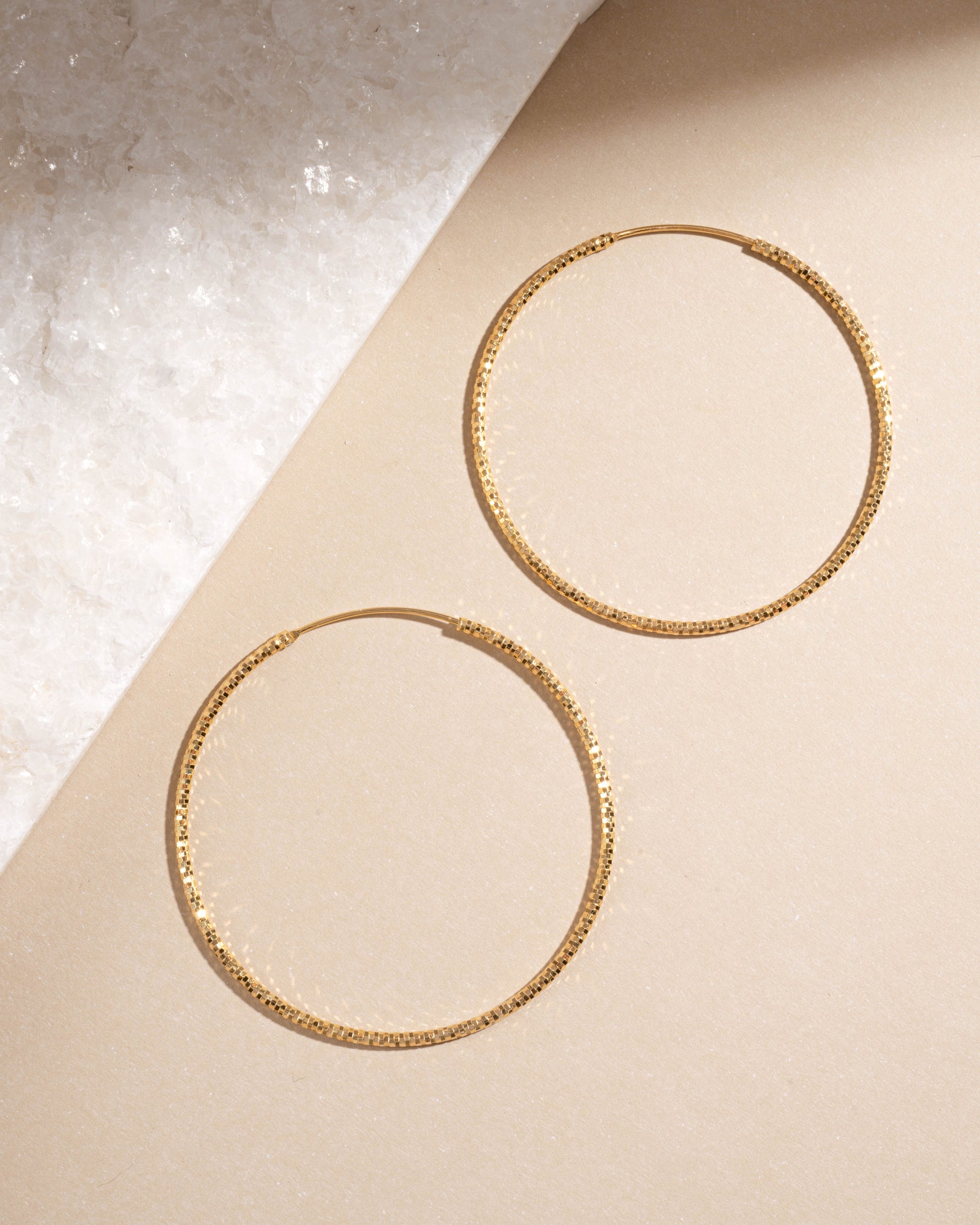 Pair of 53mm gold hoop earrings with diamond detail on a beige background