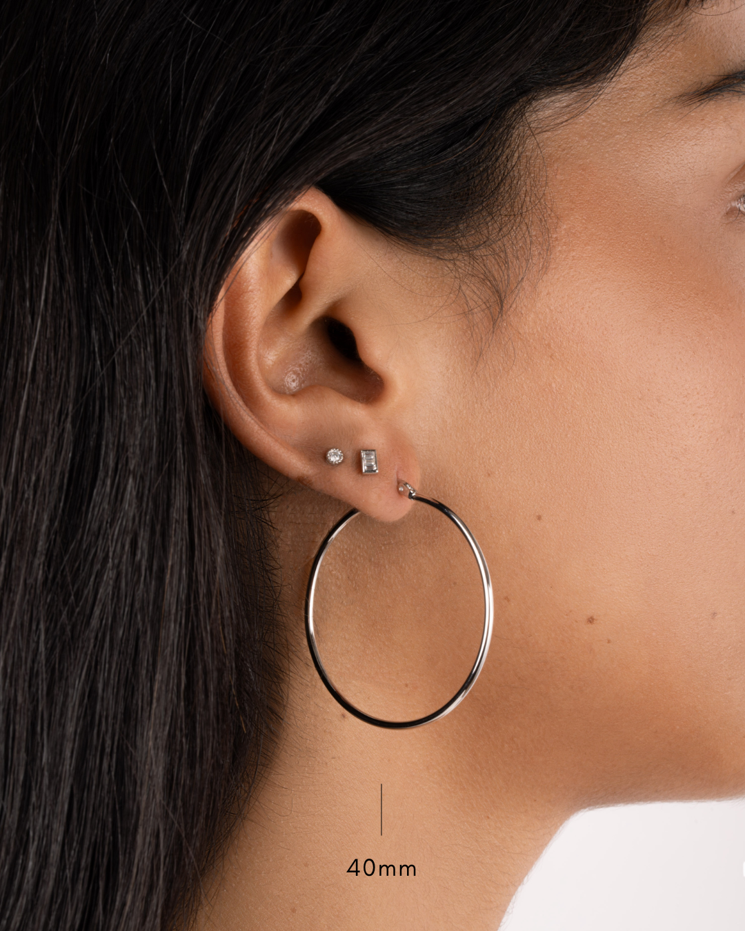 model wearing 40mm silver hoop earrings, a silver baguette stud, and a small silver bezel stud earring