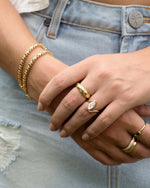 Model wearing gold stackable rings featuring a gold marquise ring, and an emerald tennis bracelet