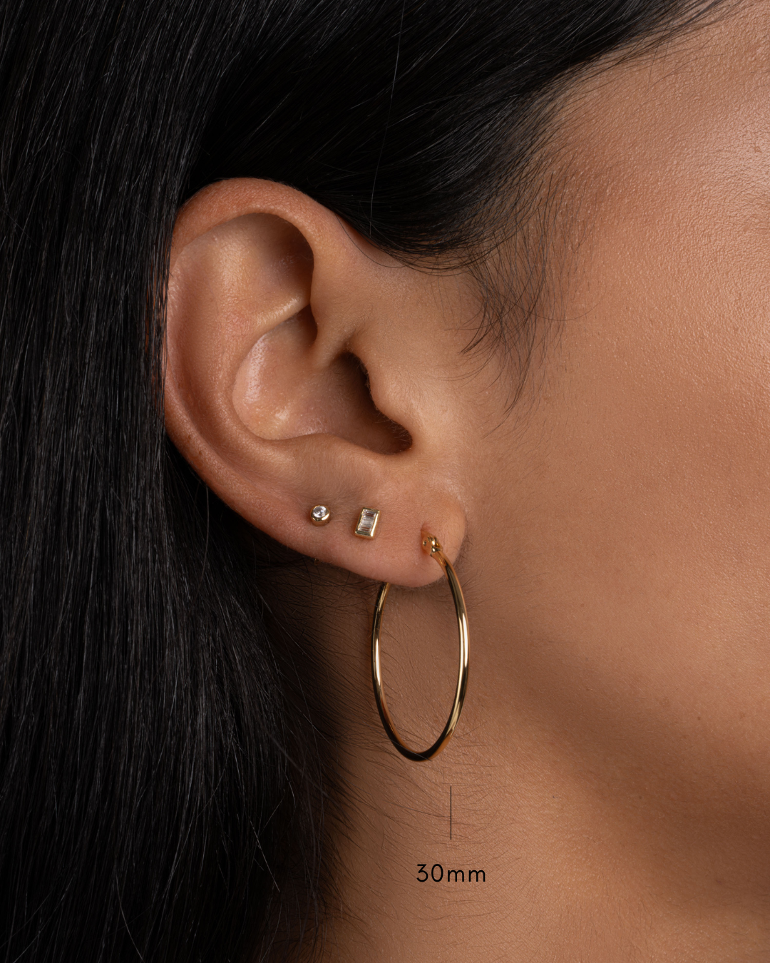 model wearing 30mm gold hoops, tiny baguette stud earrings and a tiny bezel stud earring