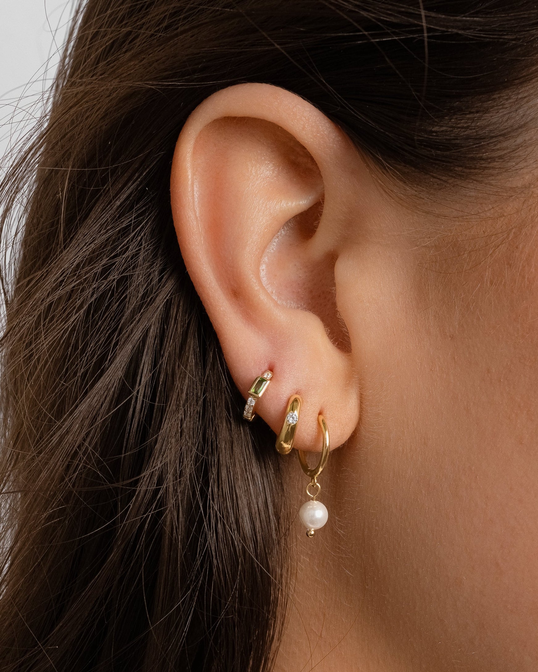model wearing gold earring stack featuring pearl drop hoops, mini dome hoops with a cz stone, and a mini hoop with cz stones