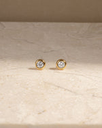Gold bezel set stud earrings with a marble background 